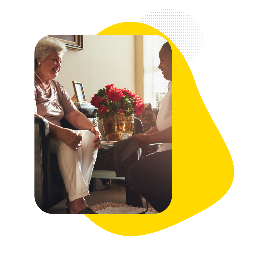 Older woman in hotel room speaking with a nurse during an in-room medical consultation.